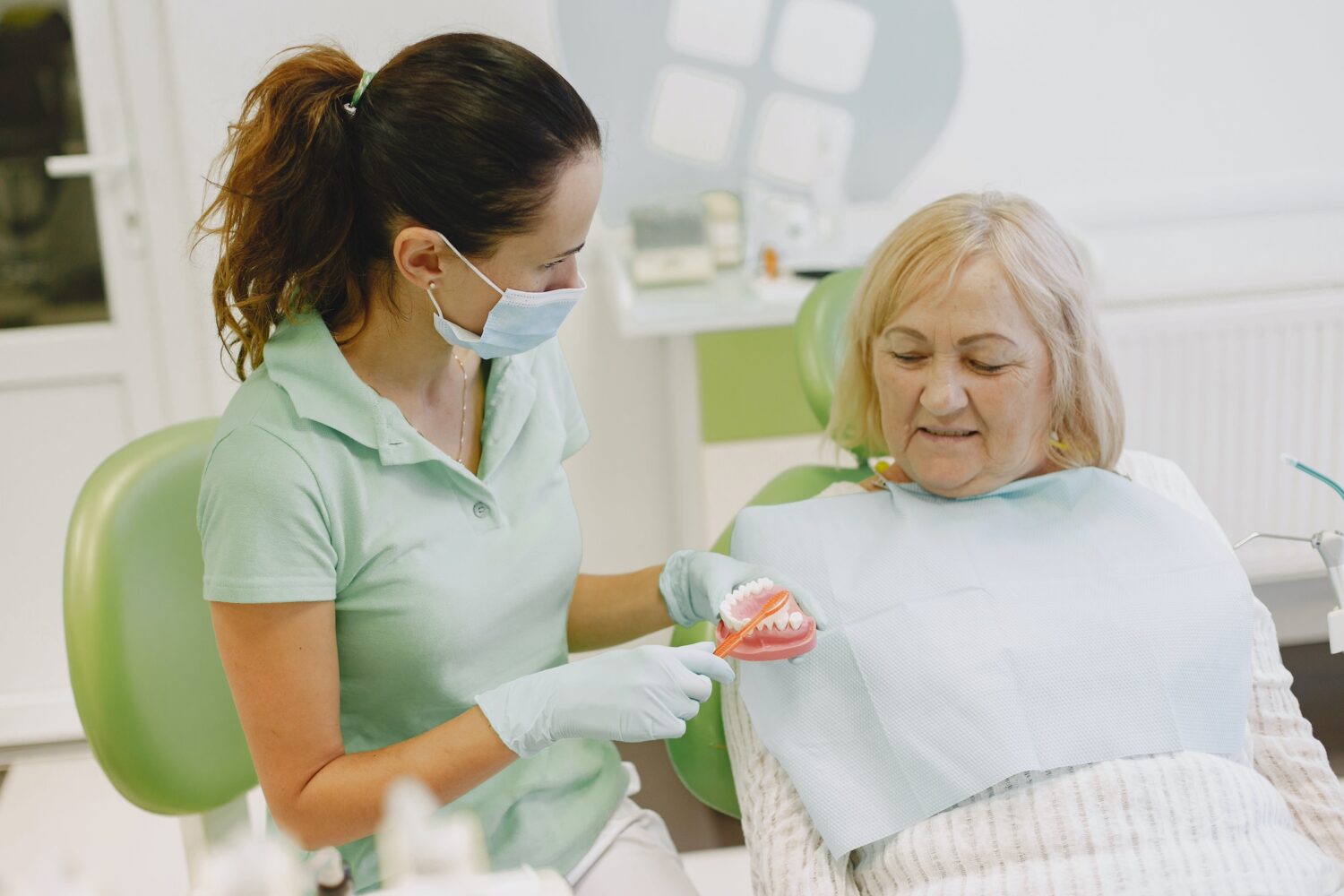 A dentist shows an elderly woman how to care for her dentures.